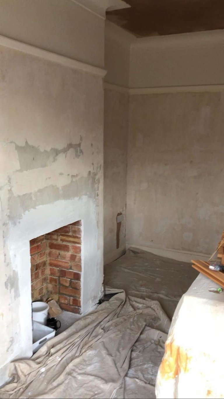 Unfinished interior room with exposed brick fireplace, plastic sheeting, and construction materials during renovation