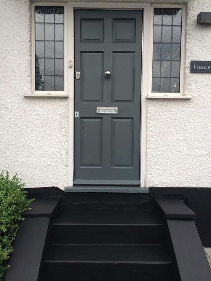 Dark gray front door with six panels on a cream-colored house facade, flanked by two sash windows and black entrance steps