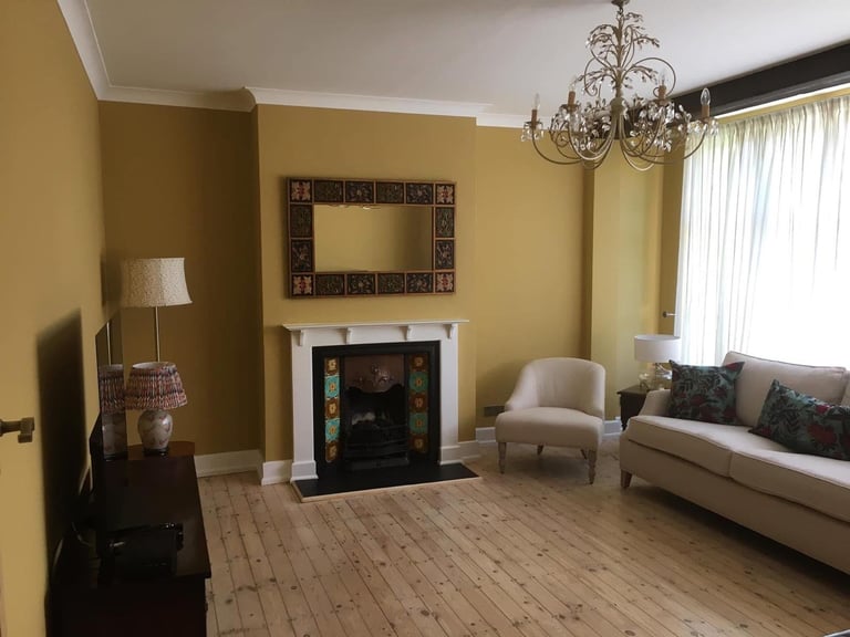 Yellow living room with fireplace, cream sofa, accent chair, chandelier, and wooden flooring