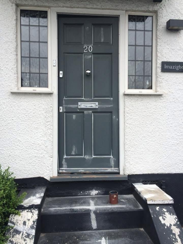 Dark green front door with number 20 on white house exterior, flanked by two tall windows